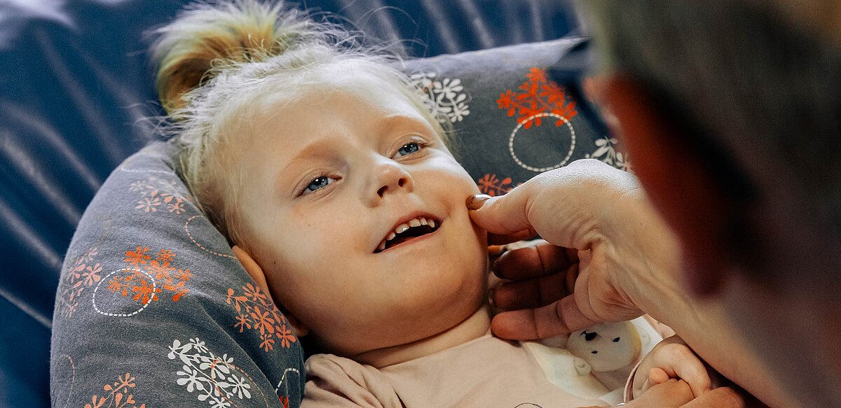 Kind liegt auf dem Rücken und sieht eine Betreuerin an. Das Kind lächelt.